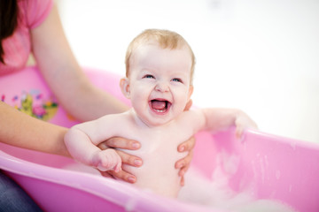 Mother washing a baby in pink bathtub