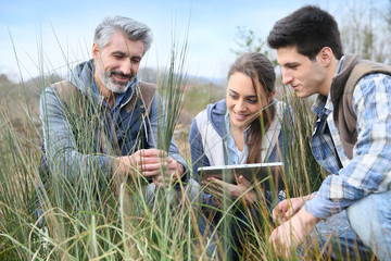 Teacher with students in agronomy looking at vegetation - obrazy, fototapety, plakaty