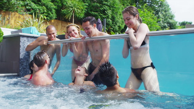 Attractive group of friends enjoy pool party and relaxing in hot tub