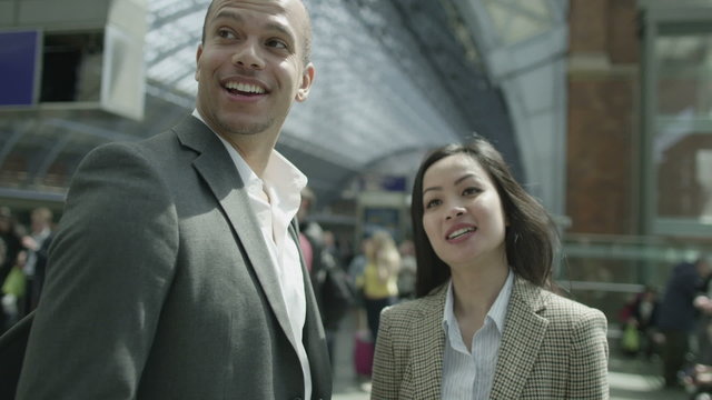 Young professionals chat while they wait for a train at a busy railway station