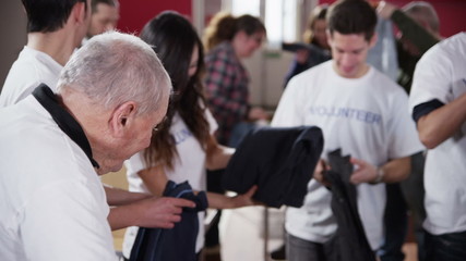 Charity volunteers in white printed t. shirts sorting through donated clothing