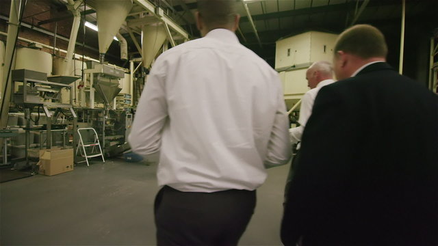 Workers in factory or warehouse walking between rows of shelves & checking stock