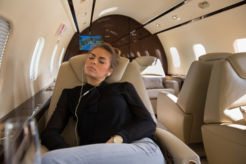 Business woman in a corporate jet relaxing and listening to musi