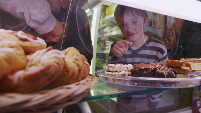 Cute little boy choosing from a selection of fresh pastries in a cafe or bakery