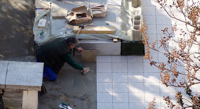 Un carreleur posant des dalles sur une terrasse