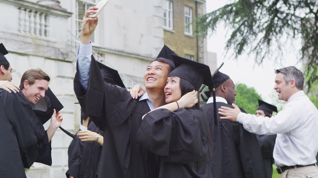 Happy student friends taking pictures of each other on graduation day