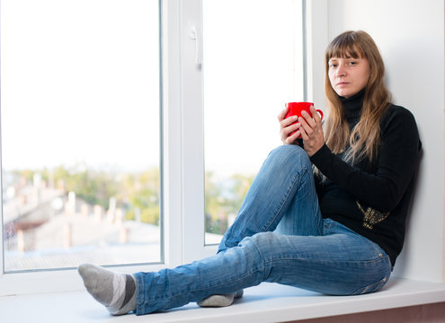 woman sitting on the window sill a cup of coffee
