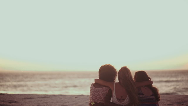 Girl friends sitting together on the beach watching the sunset