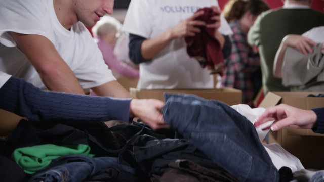 Charity volunteers in printed t. shirts sort through piles of donated clothing