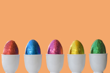 Row or line of colorful easter chocolate eggs in cups with plain orange background