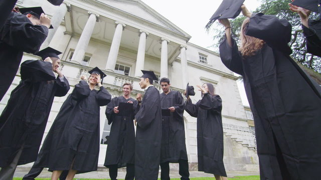 Happy group of student friends outside college building on graduation day