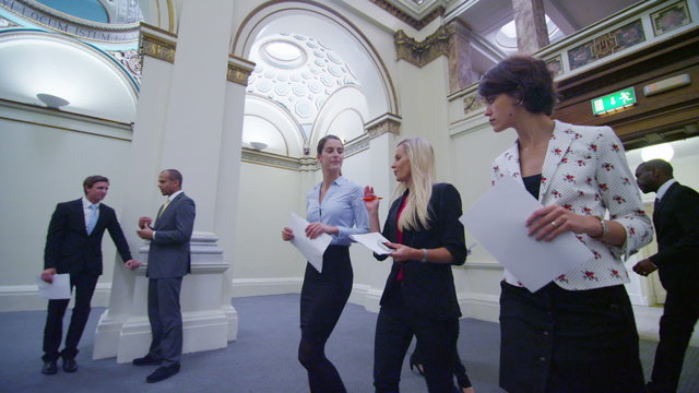 Attractive female business delegates chat as they walk through elegant building