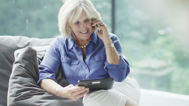 Attractive mature woman making a phone call with a computer tablet in her hand