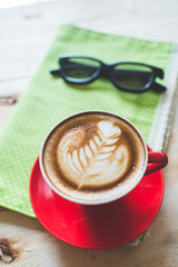 Red coffee latte art cup and glasses on wooden background.