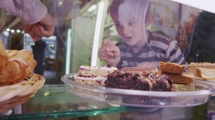 Cute little boy choosing from a selection of fresh pastries in a cafe or bakery