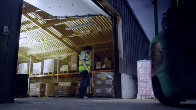 A Worker Drives A Forklift Truck Out Of A Warehouse At Night