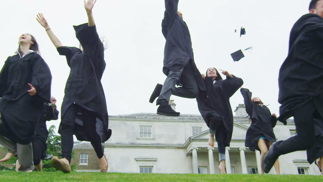 Excited students outdoors on graduation day run & jump & throw caps into the air