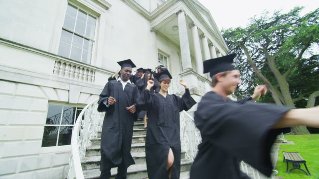 Excited students on graduation day run down a staircase outside college building