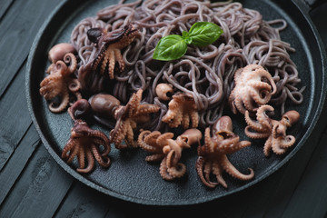 Baby octopuses with black rice noodles in a frying pan, close-up