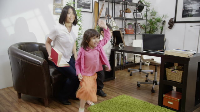 An attractive mother of Asian ethnicity is reading to her two children when their father returns home from work