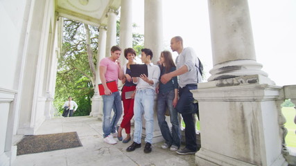 Happy group of students using tablet computer outside elegant college building