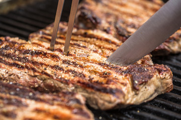 Beef steaks on grill with BBQ fork and knife