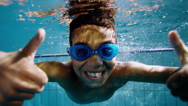 Cute little boy underwater gives a thumbs up to the camera