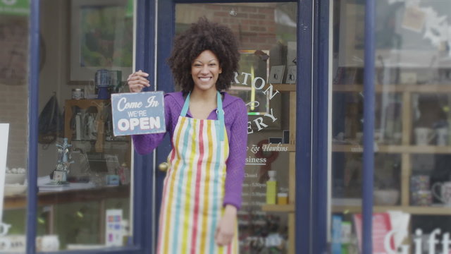 Happy female shopkeeper holds up a sign to show she is open for business