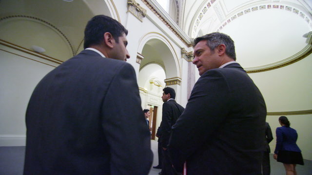 Mature male business delegates stand and chat in elegant conference building