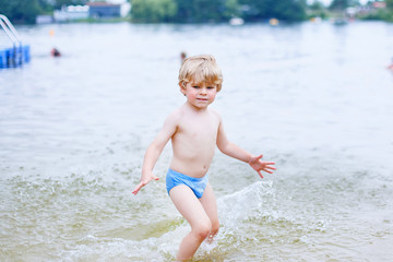 Little blond kid boy having fun with splashing in a lake, outdoo