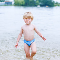 Little blond kid boy having fun with splashing in a lake, outdoo