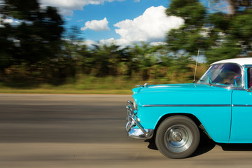 Old classic car on the road in Cuba with white clouds and blue s