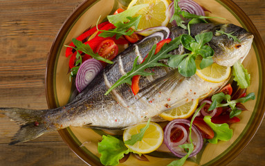 Fried dorado fish on a plate with fresh salad and lemon.