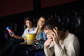 Angry Couple Looking At Man Using Mobilephone In Theater