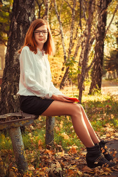 charming teen girl with red hair resting in the autumn park