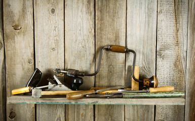 Many old tools (plane, mallet and others) on a wooden shelf.