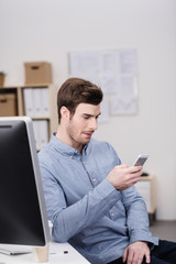 mitarbeiter im büro schaut auf sein mobiltelefon
