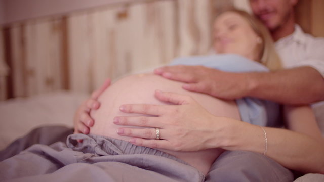 Couple touching wife's pregnant belly while lying in bed