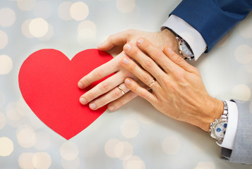 close up of male gay couple hands with red heart