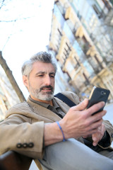 Trendy mature guy using smartphone on public bench