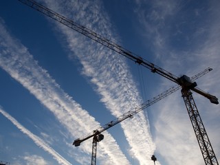 Obraz premium Two construction cranes against the sky and clouds