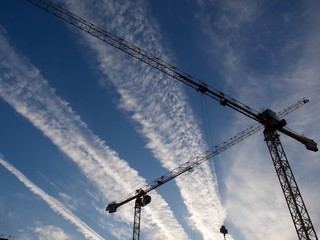 Two construction cranes against the sky and clouds