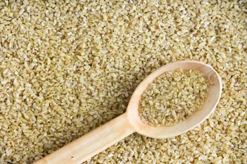 Healthy cracked wheat and spoon background texture