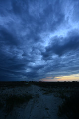 dark storm clouds above sand road in steppe landscape at sunset