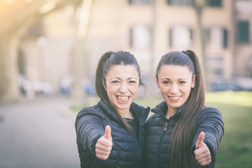 Happy female twins showing thumbs up at park