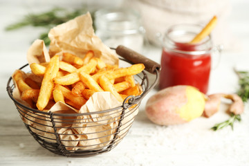 Tasty french fries in metal basket on color wooden background