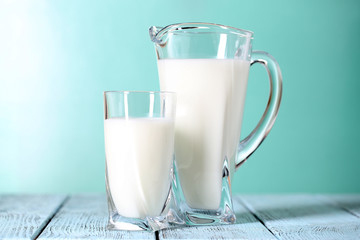 Pitcher and glass of milk on wooden table on blue background