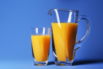 Glass and pitcher of orange juice on blue background