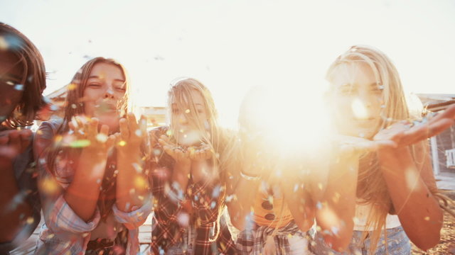 Teen friends blowing colorful confetti on sunny summer evening