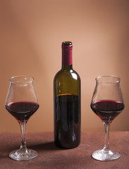 Red wine bottle and two filled wineglasses on brown background